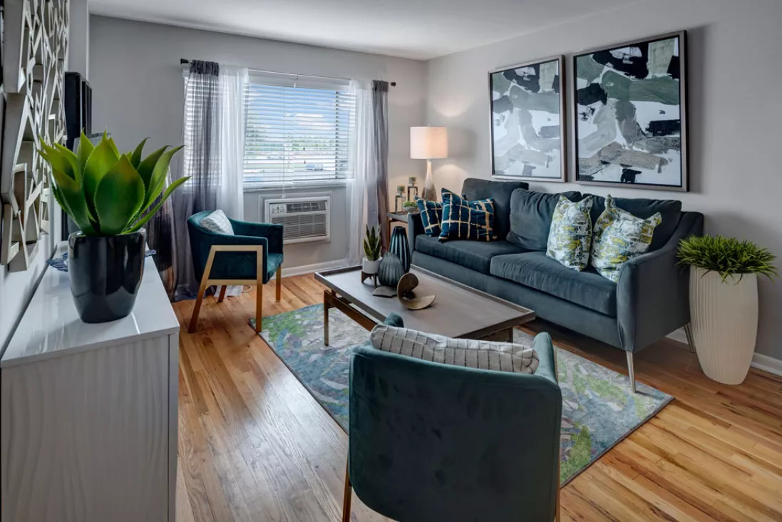 Modern living room with a dark blue sofa, teal armchairs, abstract wall art, and a patterned rug on hardwood floors.