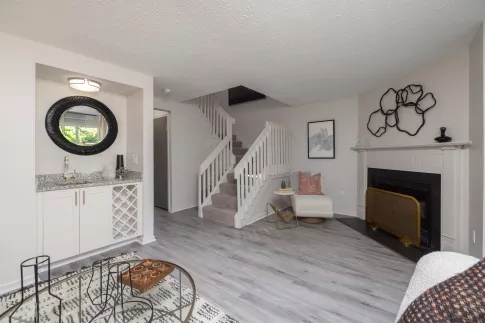 Spacious living room featuring a built-in bar, a central staircase, and a fireplace with a brass screen.