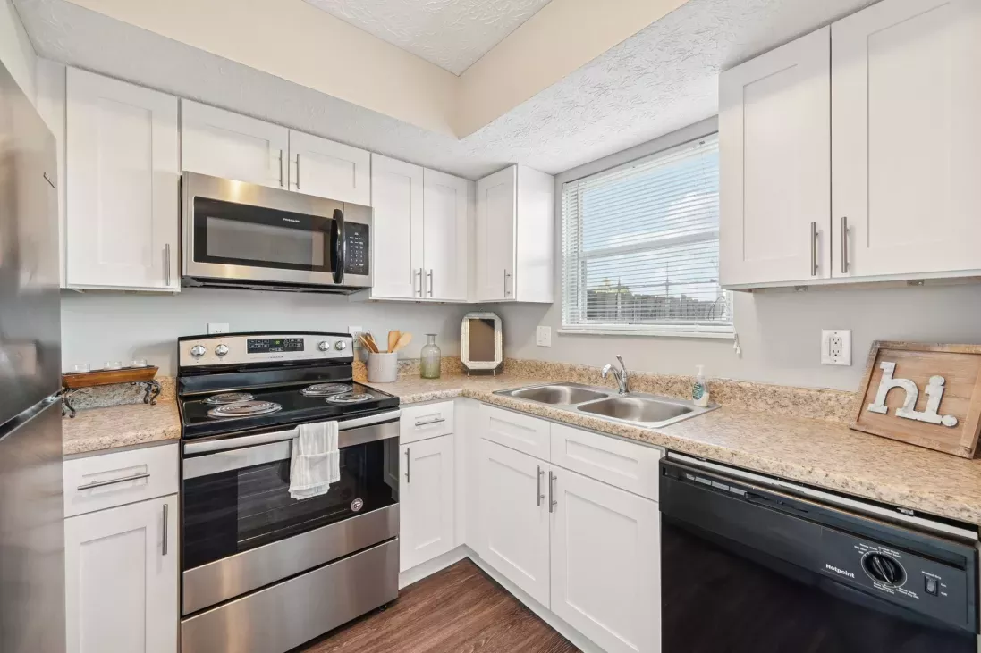 Modern kitchen with white cabinets, stainless steel microwave and oven, speckled counters, and black dishwasher.