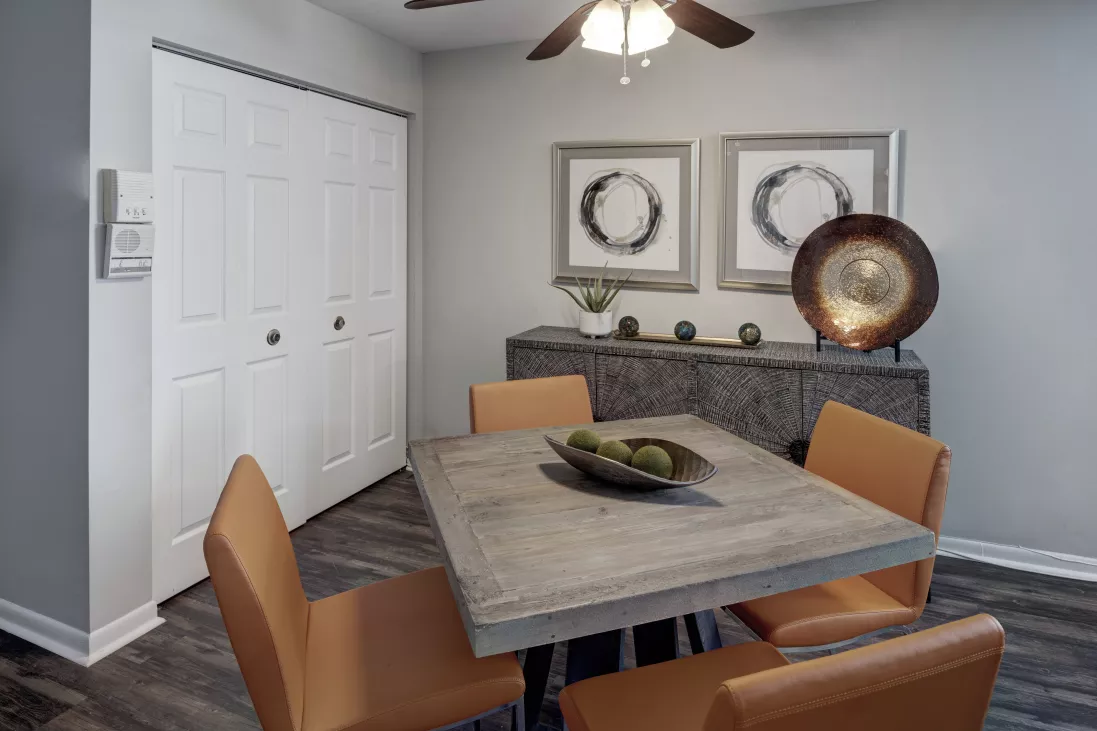 Dining area with square wooden table, four orange chairs, console table with decor, and framed art.