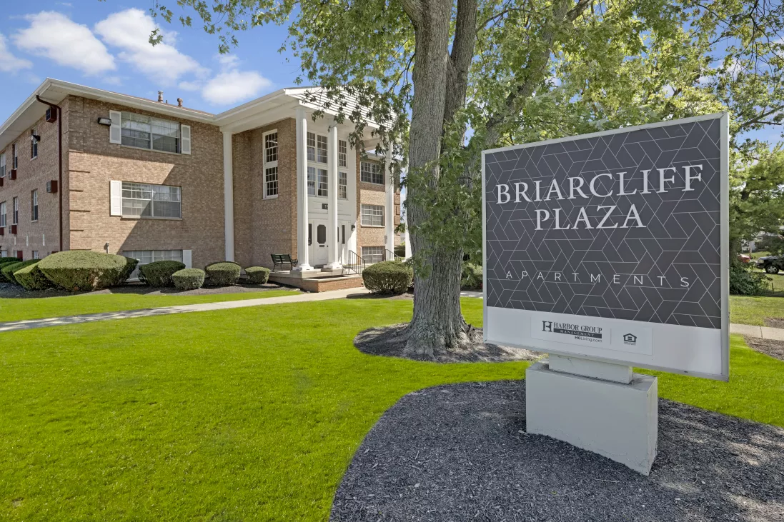 Briarcliff Plaza Apartments sign on a green lawn, with a tan brick building and white columns in the background.