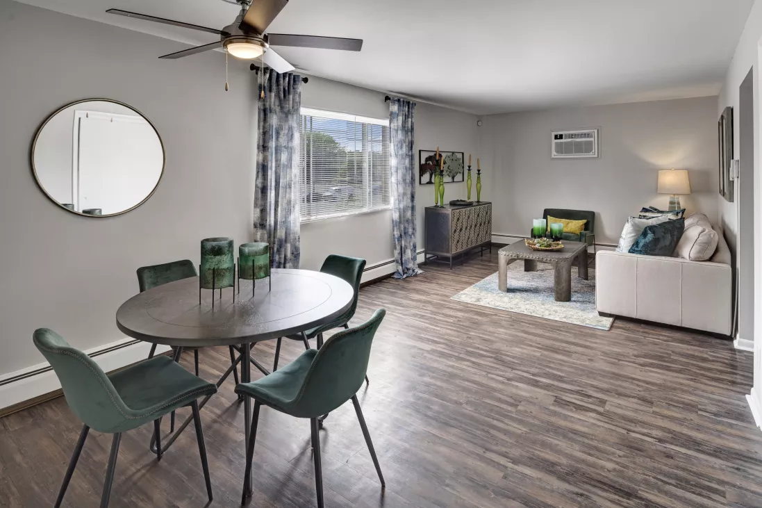 Modern apartment living and dining area with a round table, green chairs, sofa, coffee table, and dark wood floors.