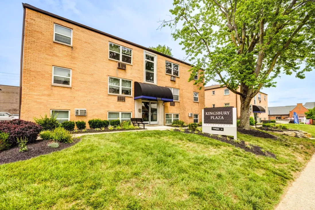 Three-story brick apartment building with blue awning over entrance, green lawn, and "CHERRY ARMS PLAZA" sign.