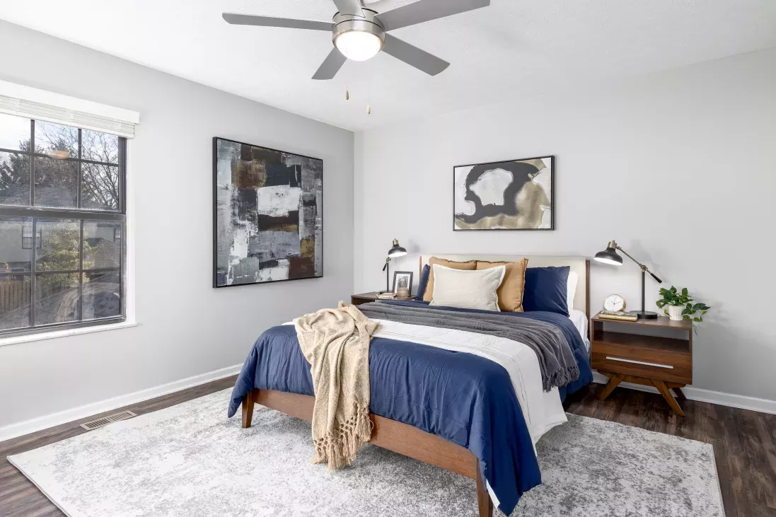 Modern bedroom with a bed, navy duvet, shaggy white rug, light gray walls, and abstract art. Wooden nightstand with lamp.