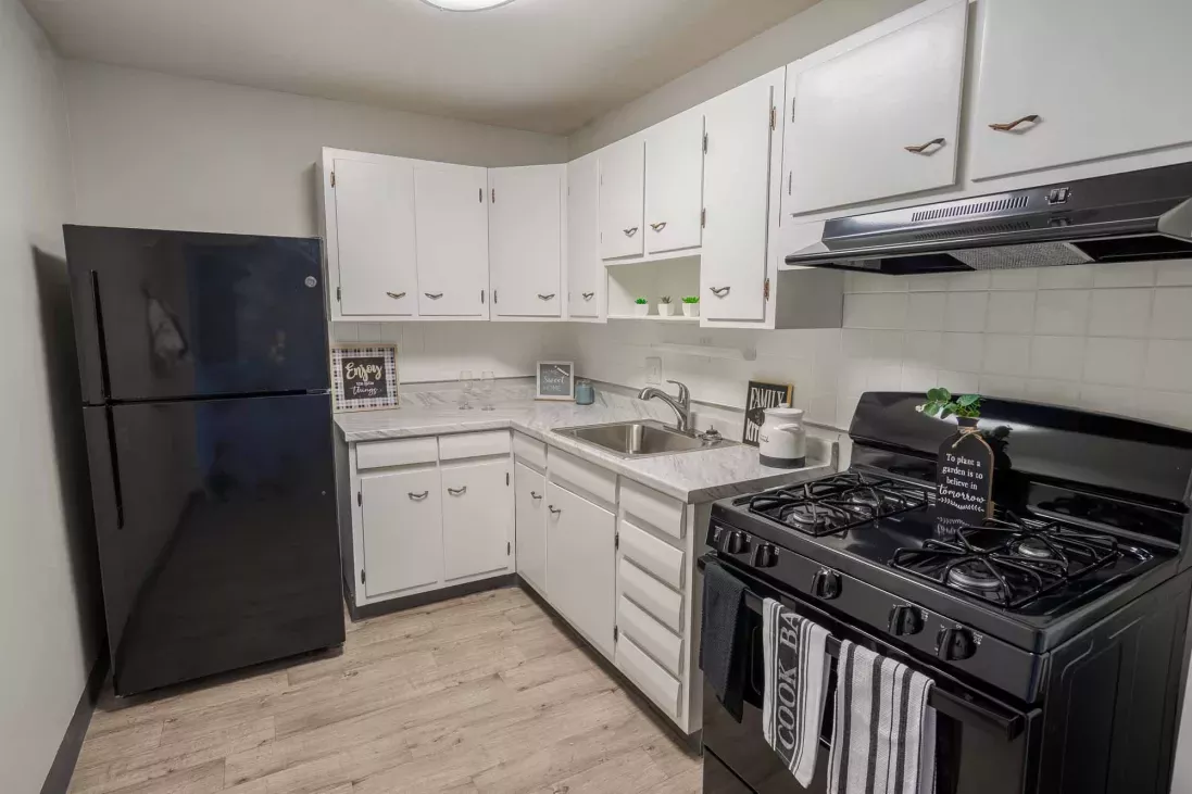 Compact kitchen with white upper and lower cabinets, black appliances, and light wood-look flooring.