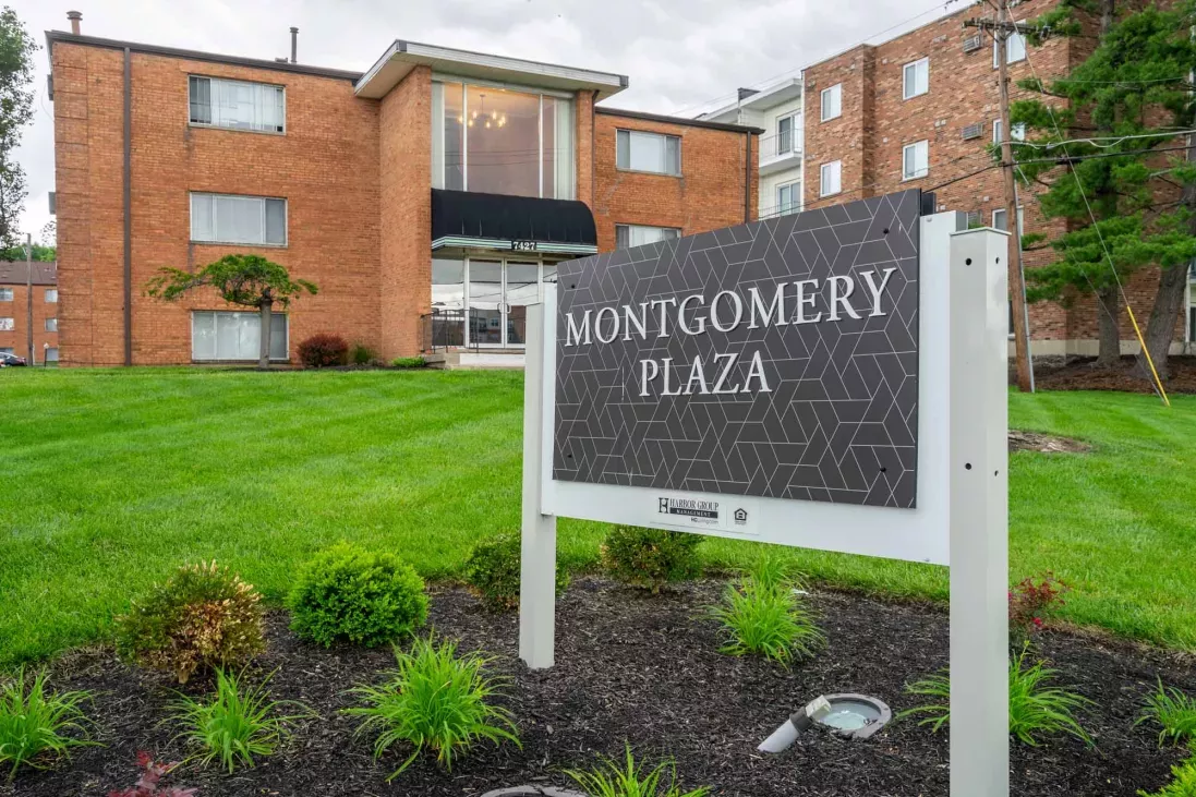 Photograph of a Montgomery Plaza sign in front of a red brick apartment building with green grass.