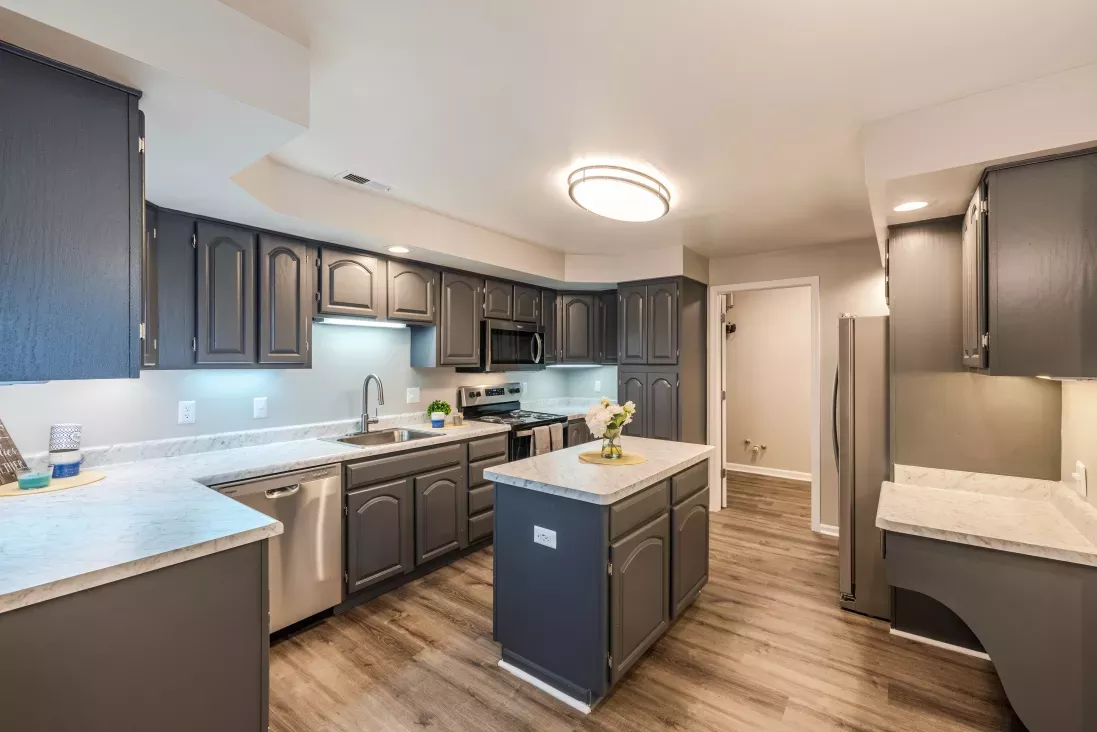 Modern kitchen with dark gray cabinets, light countertops, wood-look floor, island, and stainless steel appliances.