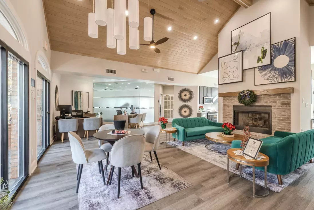 Apartment complex lobby with vaulted wood ceilings, a fireplace, teal sofas, and holiday decorations.
