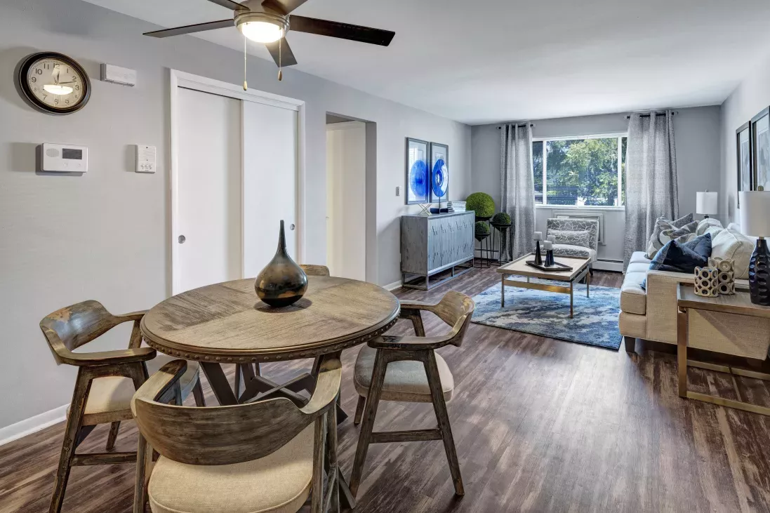 Furnished apartment living room with a round wooden dining table, three chairs, a white couch, coffee table, and window.