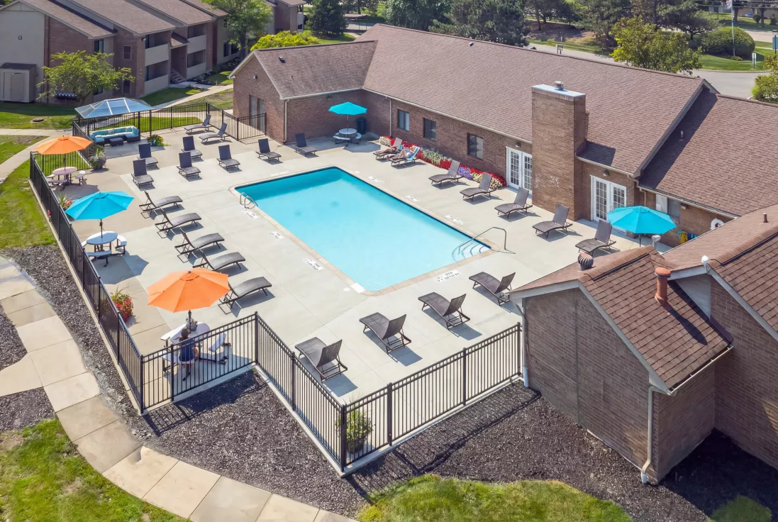 Aerial photograph of an outdoor swimming pool with lounge chairs, colorful umbrellas, and an adjacent brick building.