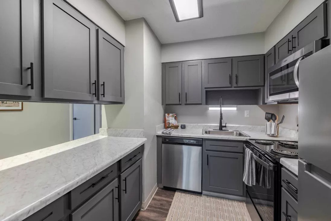 Modern kitchen with dark gray cabinets, white countertops, stainless steel appliances, and wood flooring.