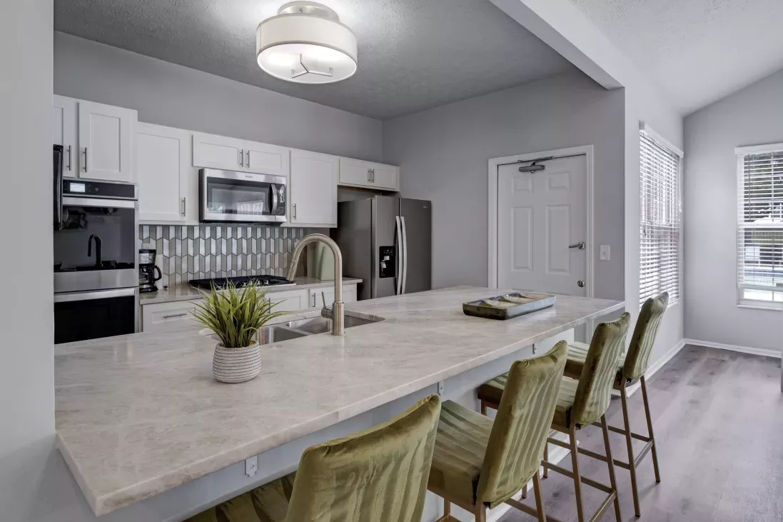 Modern kitchen with white cabinets, light countertops, green bar stools, stainless steel appliances, and a unique tiled backsplash.