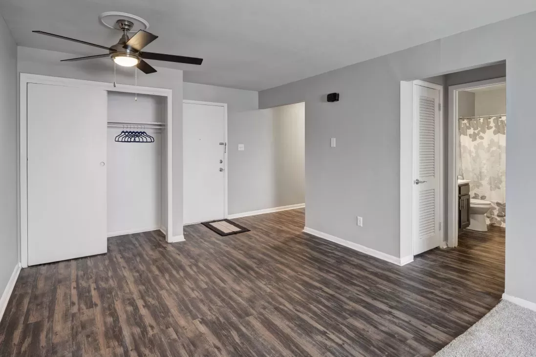 Empty room with gray walls, dark wood floor, open closet, ceiling fan, and visible bathroom.