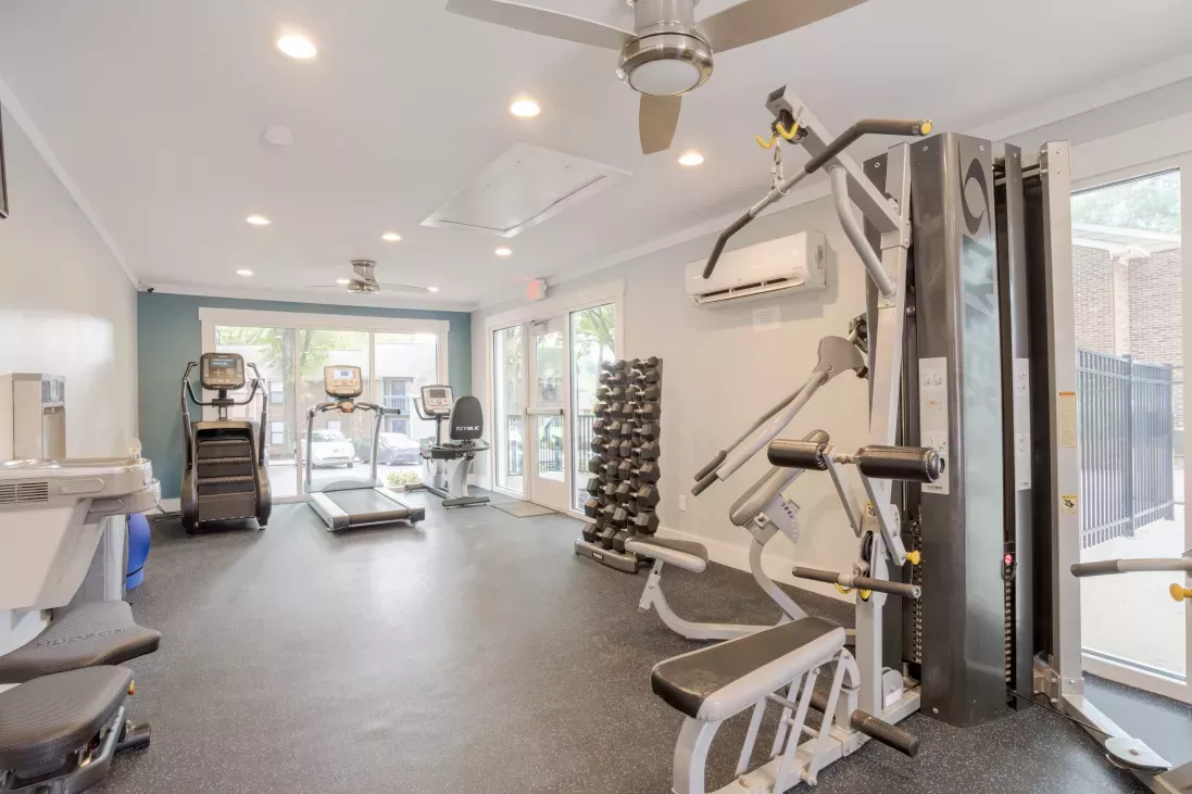 Photograph: Bright gym with treadmills, elliptical, weight machines, and dumbbells on dark flooring, large windows.