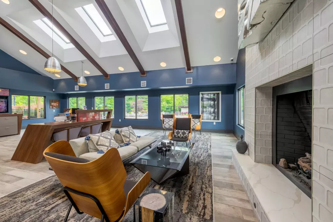 Spacious, modern lounge with blue walls, vaulted ceiling, skylights, a large fireplace, white sofa, and an orange armchair.