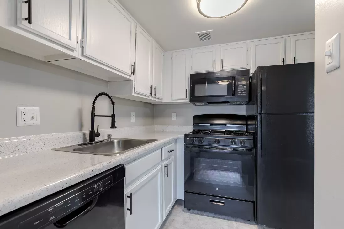 Modern kitchen with white cabinets, light gray countertops, and black appliances including a fridge, stove, and dishwasher.