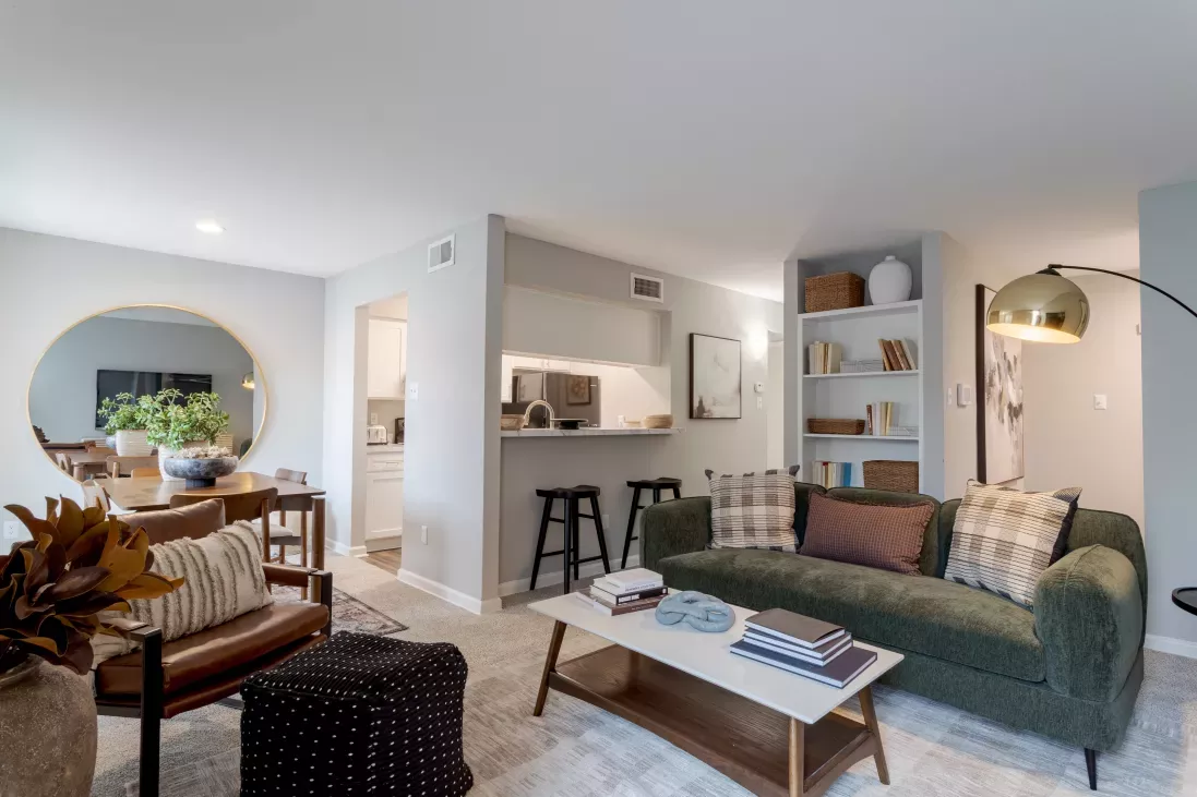 Stylish living room with a green sofa, coffee table, bar counter with stools, and a large round mirror.