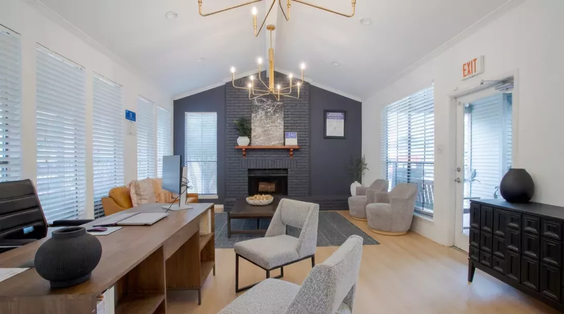 Bright, modern common area with high ceilings, chandelier, dark blue fireplace, wood desk, and various lounge seating.