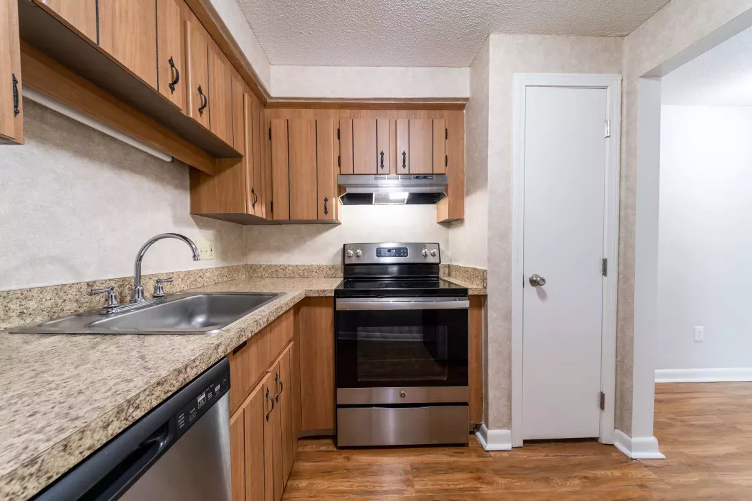 Kitchen with light wood cabinets, speckled countertops, stainless steel stove, sink, and dishwasher, plus a wood floor.