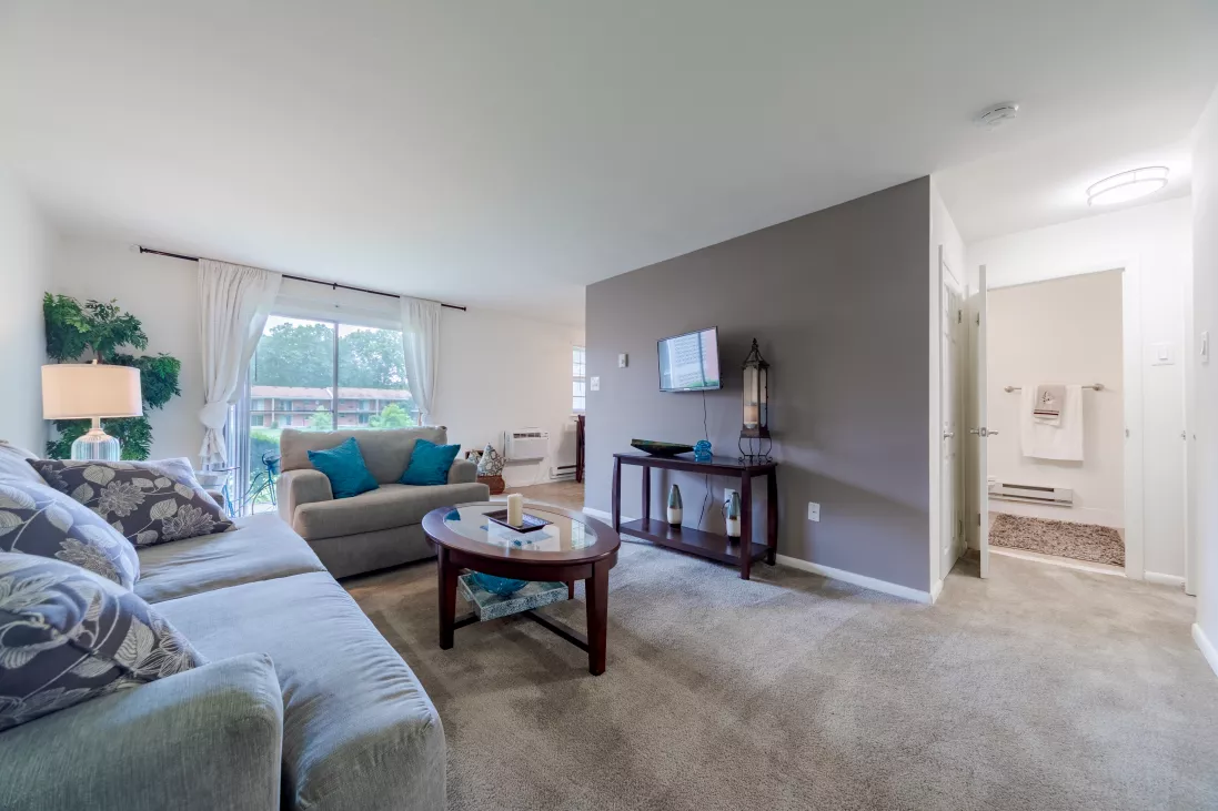 Cozy living room with beige sofas, blue throw pillows, coffee table, TV on gray accent wall. Bathroom entrance.