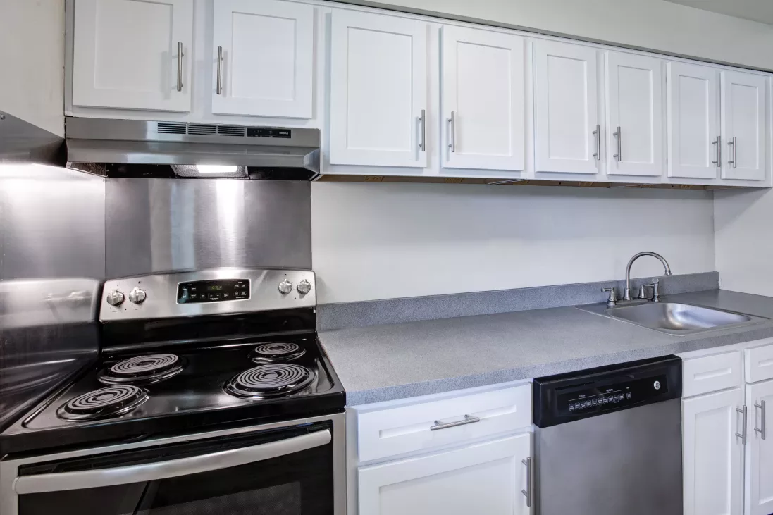 Kitchen with white upper cabinets, stainless steel electric range, dishwasher, and grey countertops with a sink.