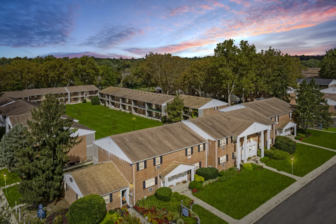 Aerial view of a complex with two-story brick buildings, green lawns, trees, and a colorful sunset sky.