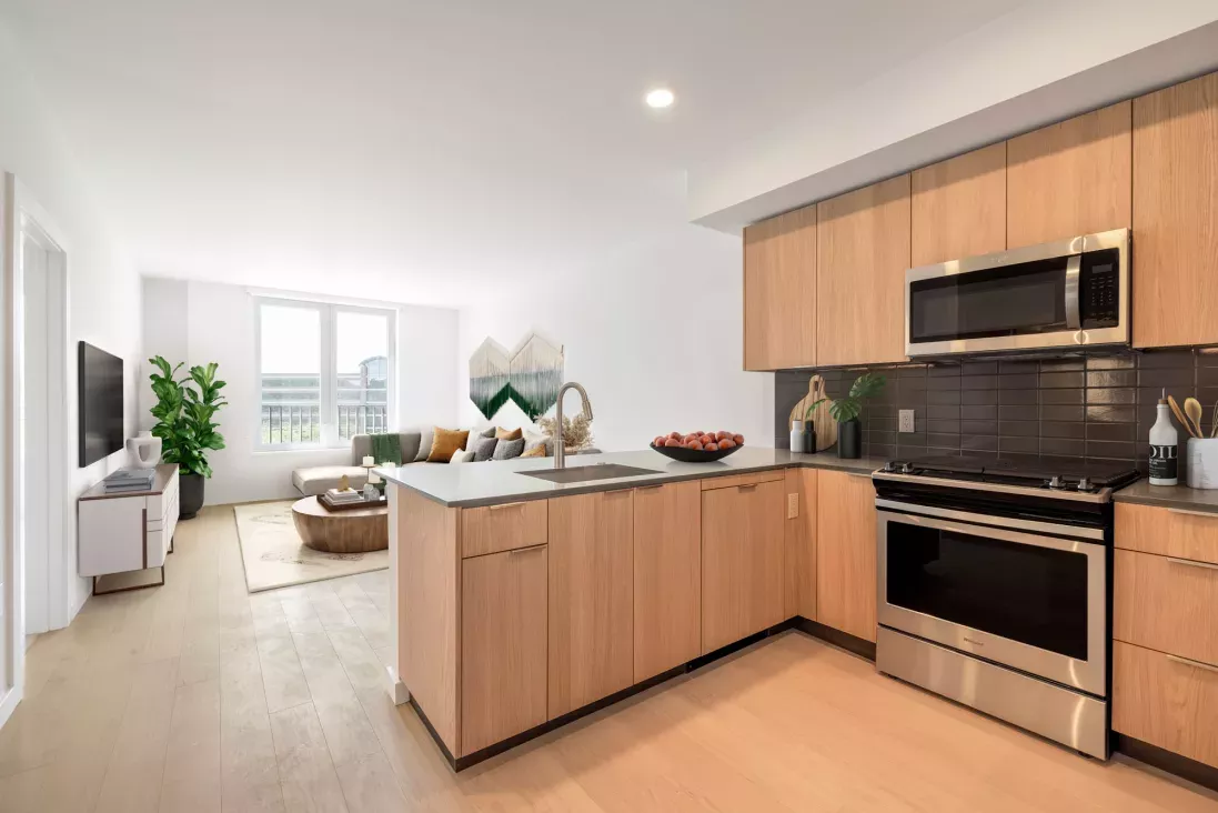 Modern kitchen featuring stainless steel appliances, wood cabinetry, and a sleek tile backsplash at The Edmund Apartments.