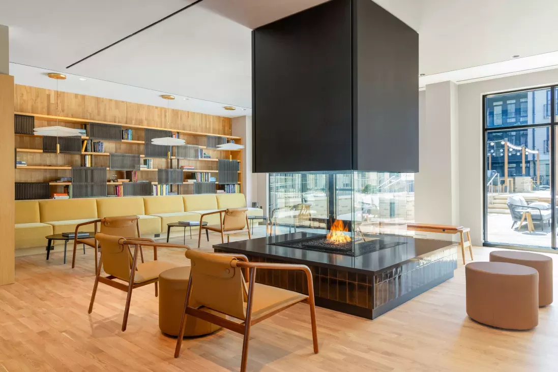 An inviting common area with a glass-encased central fireplace, ample seating, and an outdoor view, blending luxury and comfort for social gatherings.