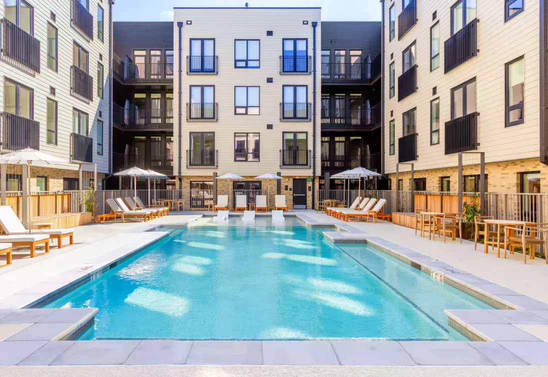 Outdoor pool area at The Edmund Apartments featuring lounge chairs, umbrellas, and in-pool seating surrounded by modern apartment buildings.