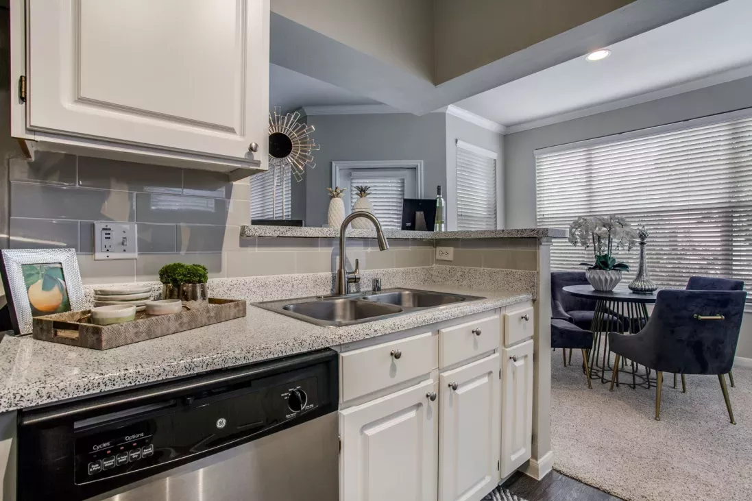 Modern kitchen with granite countertops, stainless steel appliances, and an open concept design leading into a brightly lit living room with large windows at Arboretum Estates.