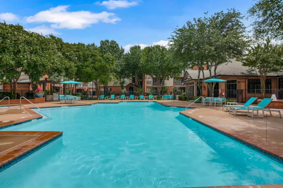 Sparkling resort-style swimming pool surrounded by lounge chairs, umbrellas, and lush greenery, offering a relaxing retreat at Arboretum Estates.