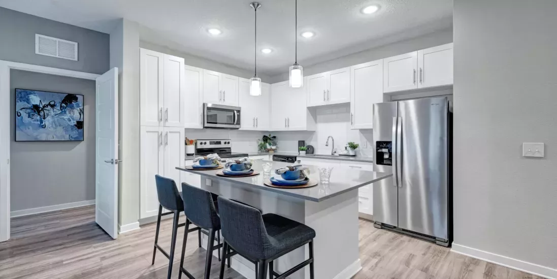 A modern kitchen with white cabinetry, stainless steel appliances, a sleek island with bar seating, and a contemporary dining setup.