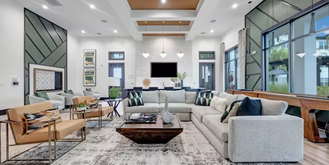 A spacious clubhouse lounge with stylish furniture, pendant lighting, large windows, and a sophisticated design.