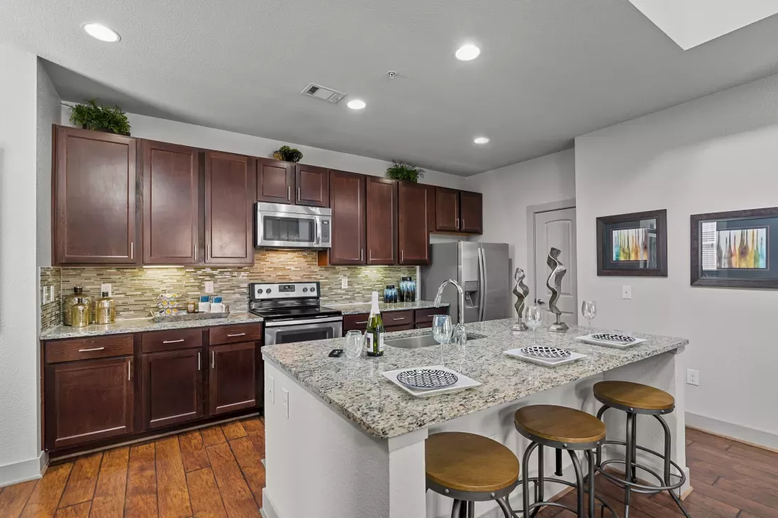 A modern kitchen with stainless steel appliances, dark wood cabinetry, granite countertops, and a large island with barstools.