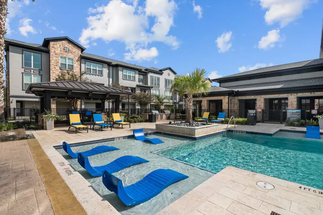 A luxurious outdoor pool area with blue lounge chairs, a shaded cabana, and resort-style landscaping.
