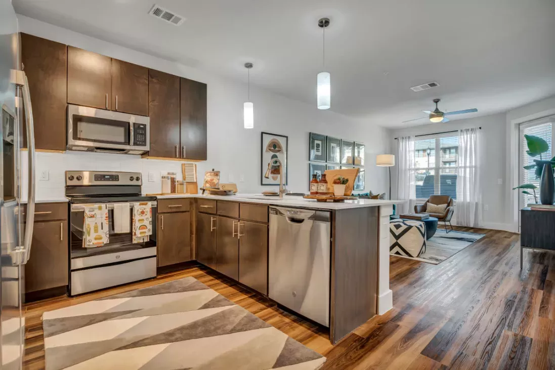 A modern kitchen with dark wood cabinets, stainless steel appliances, and a bright, open layout connecting to the living space.