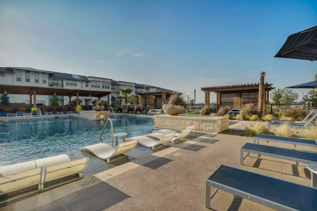 A serene outdoor pool with sun loungers and shaded pergolas, surrounded by landscaping.
