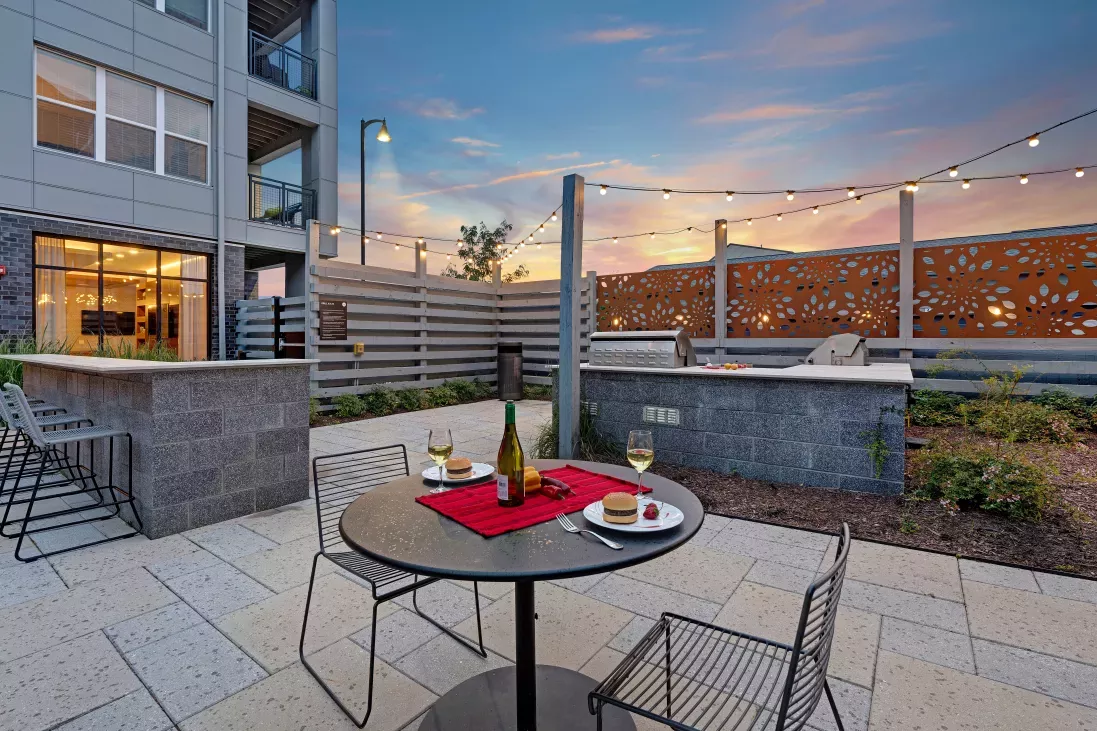 A beautifully lit patio space with a stainless steel grilling station, stylish seating, and a modern privacy screen, perfect for al fresco dining and evening entertainment.