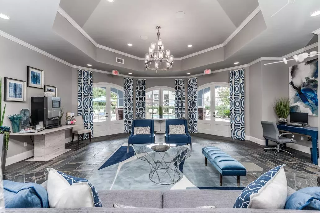 Elegant and inviting resident lounge with bold blue decor, a stunning chandelier, and access to the pool area at The Landings of Conroe.