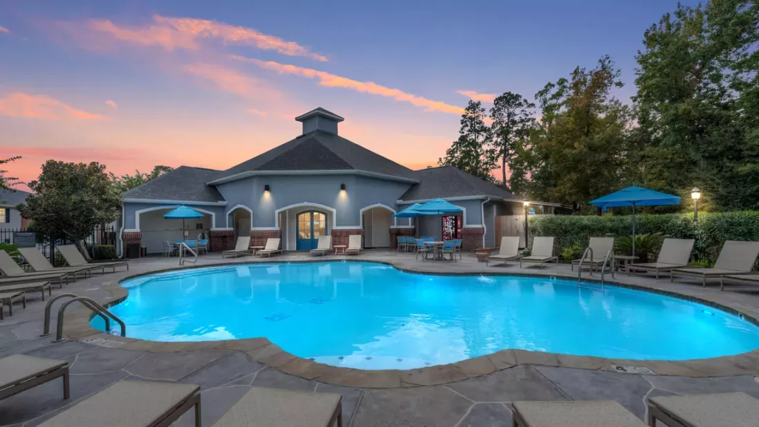 Resort-style pool at The Landings of Conroe Luxury Apartments with comfortable seating, umbrellas, and a serene evening ambiance.