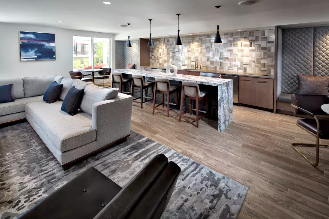 A stylish resident lounge with a sleek marble island, bar seating, cozy sectional sofa, and modern lighting at The Mark at Mamaroneck Luxury Apartments.