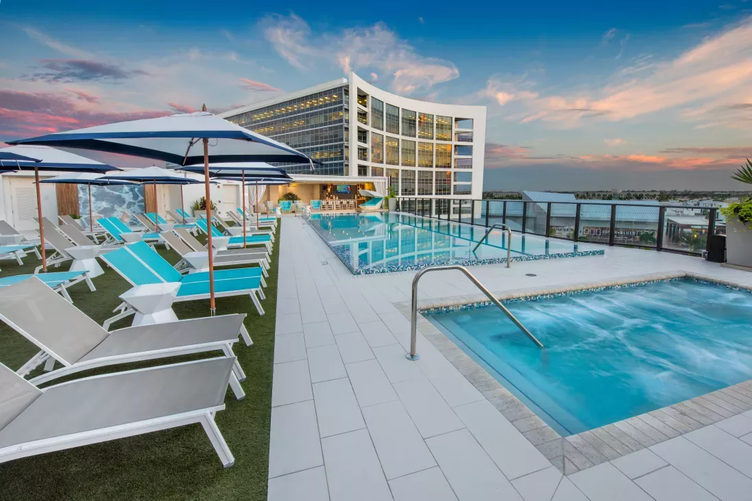 Rooftop pool at The Flats at City Place Luxury Apartments with modern lounge chairs, shaded cabanas, and stunning sunset views over the city skyline.