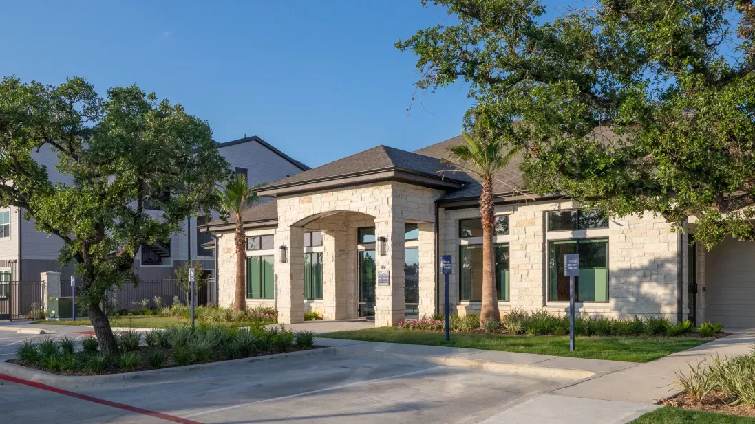 The leasing office exterior features a modern design with a stone facade, arched entryway, and lush landscaping, creating an inviting welcome to Vista At Town Green Luxury Apartments.