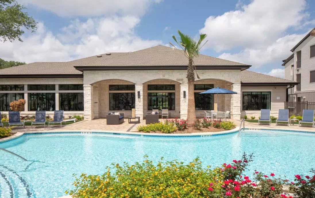 The resort-style pool area is surrounded by lounge chairs, lush landscaping, and an elegant clubhouse, offering a perfect retreat for relaxation and outdoor enjoyment.