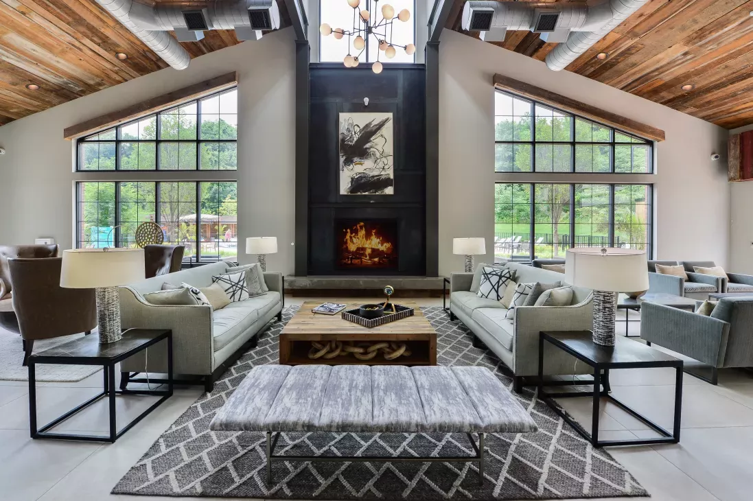 Elegant clubhouse interior with high ceilings, a warm fireplace, contemporary furnishings, and large windows showcasing serene outdoor views.