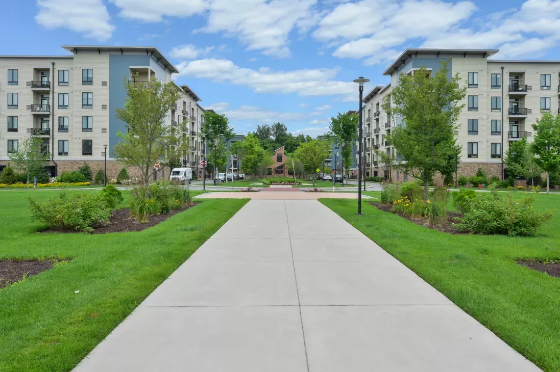Expansive courtyard with beautifully landscaped gardens, wide walkways, and contemporary apartment buildings framing a scenic central green space.