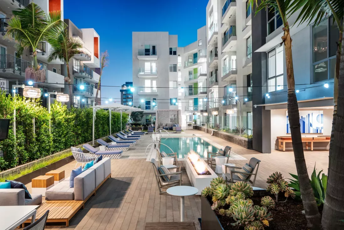 Resort-style pool area at The Linden Luxury Apartments showcasing lounge seating, ambient lighting, and a beautiful fire pit surrounded by lush greenery.