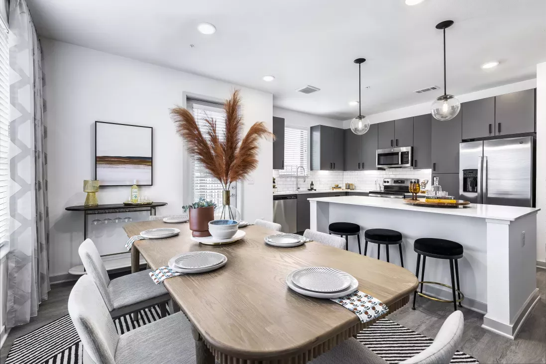 A stylish open-concept kitchen and dining area at The Warner Apartments, featuring sleek gray cabinetry, stainless steel appliances, and a beautifully set dining table with contemporary decor.