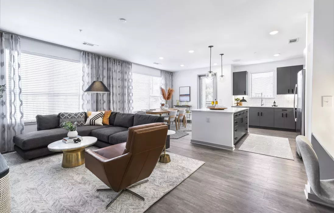 A luxurious open living space at The Warner Apartments, combining a cozy sectional sofa, elegant dining area, and a modern kitchen with pendant lighting and upscale finishes.