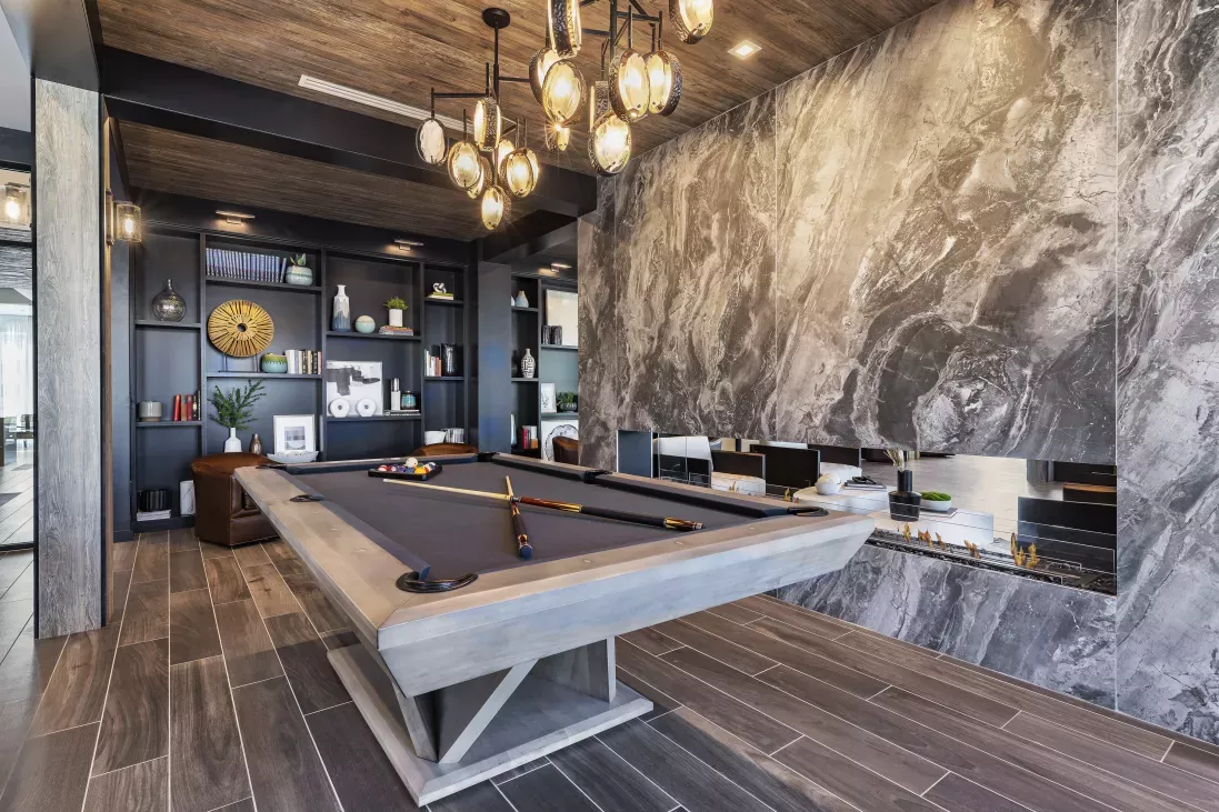 A sophisticated resident game room at The Warner Apartments, featuring a contemporary pool table, built-in bookshelves, and a sleek fireplace for a relaxing and social atmosphere.